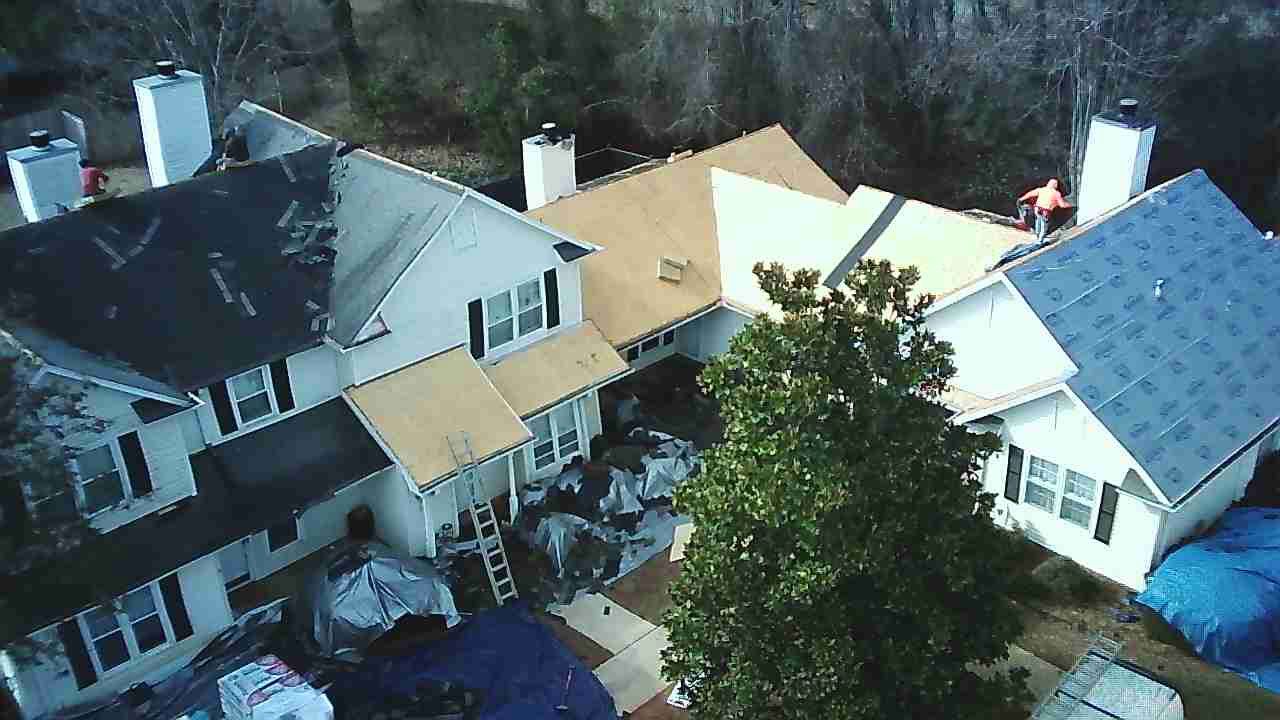 An aerial view of a house during a roof replacement, with workers on the roof sections covered in underlayment.