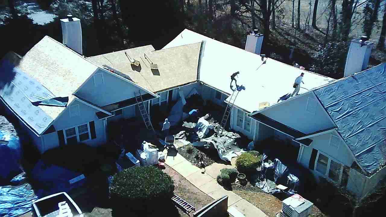 Aerial view of construction workers installing new roofing shingles on a residential house during a renovation.