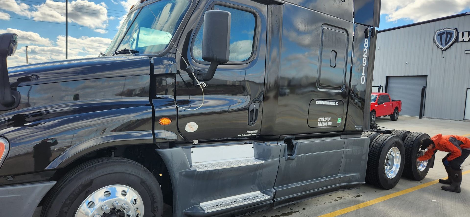 a black semi truck is parked in a parking lot next to a building .