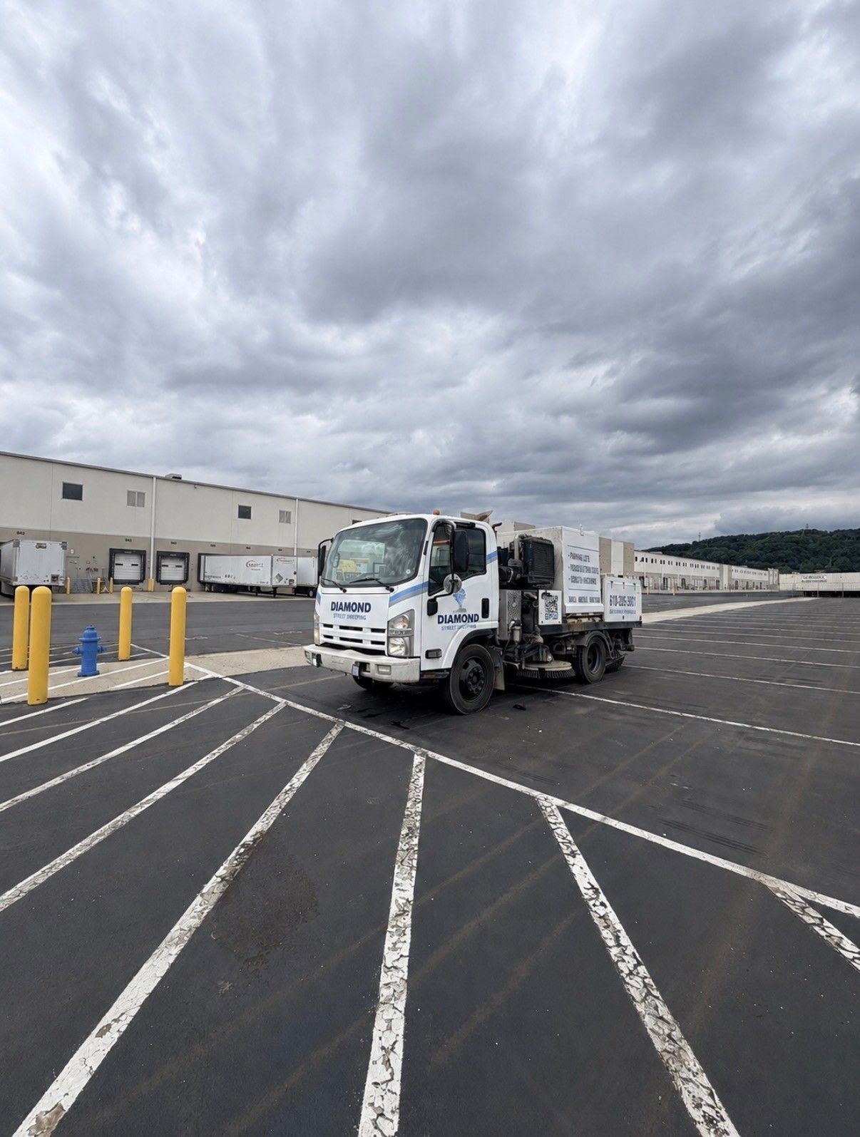 White utility truck parked in an empty lot under cloudy skies beside a warehouse building