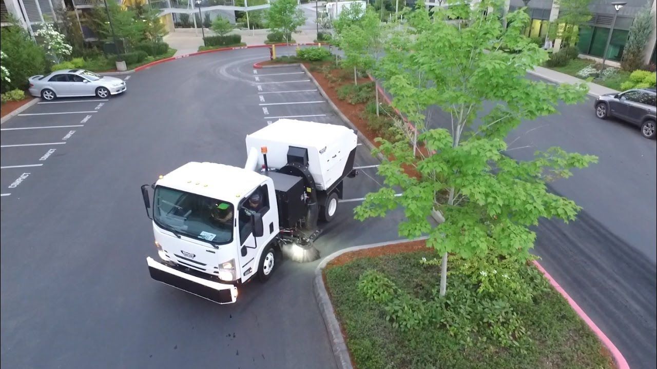 White utility truck turning into a parking lot beside trees and parked cars.