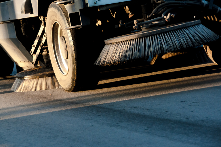 Street sweeper cleaning pavement with spinning brushes at road level