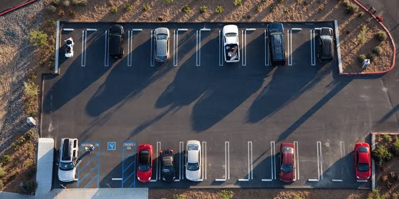Aerial view of a parking lot with several parked cars in marked spaces and long shadows.