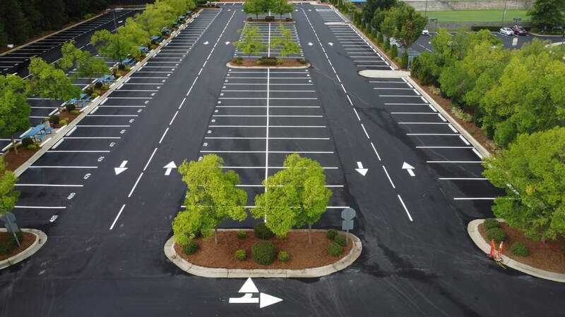 Empty parking lot with newly planted trees in raised islands and white directional arrows on dark pavement