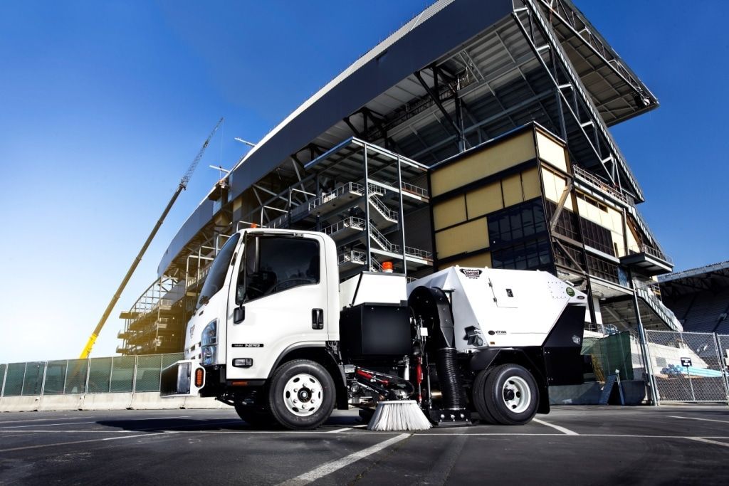 White garbage truck parked outside a stadium under a clear blue sky