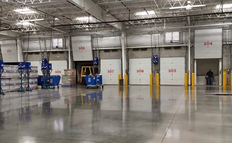 Empty warehouse loading area with blue shelving, yellow bollards, and red numbered dock doors.