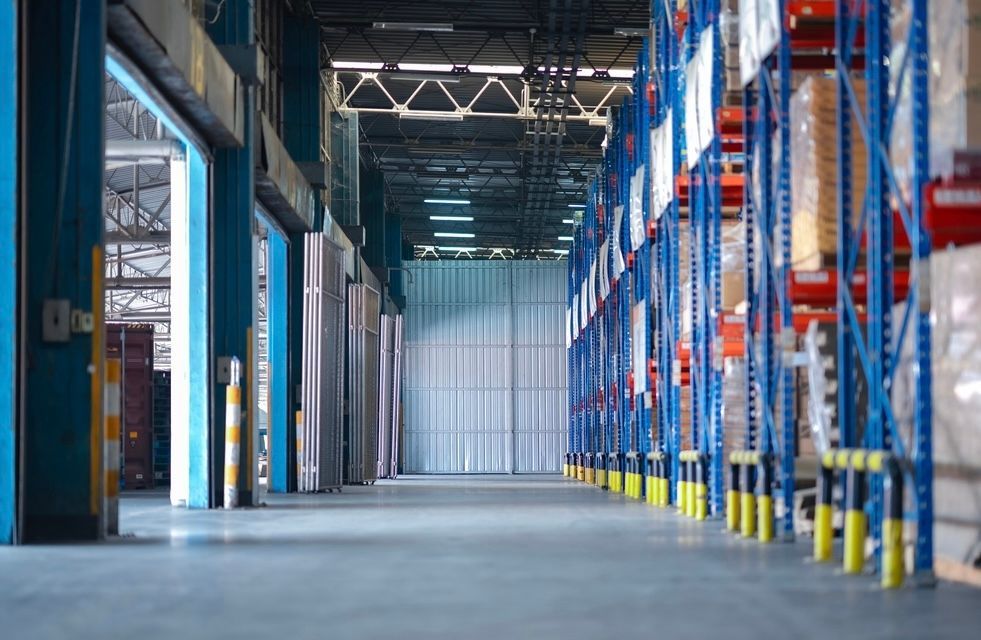 Empty warehouse aisle with blue and orange storage racks along a wide concrete floor