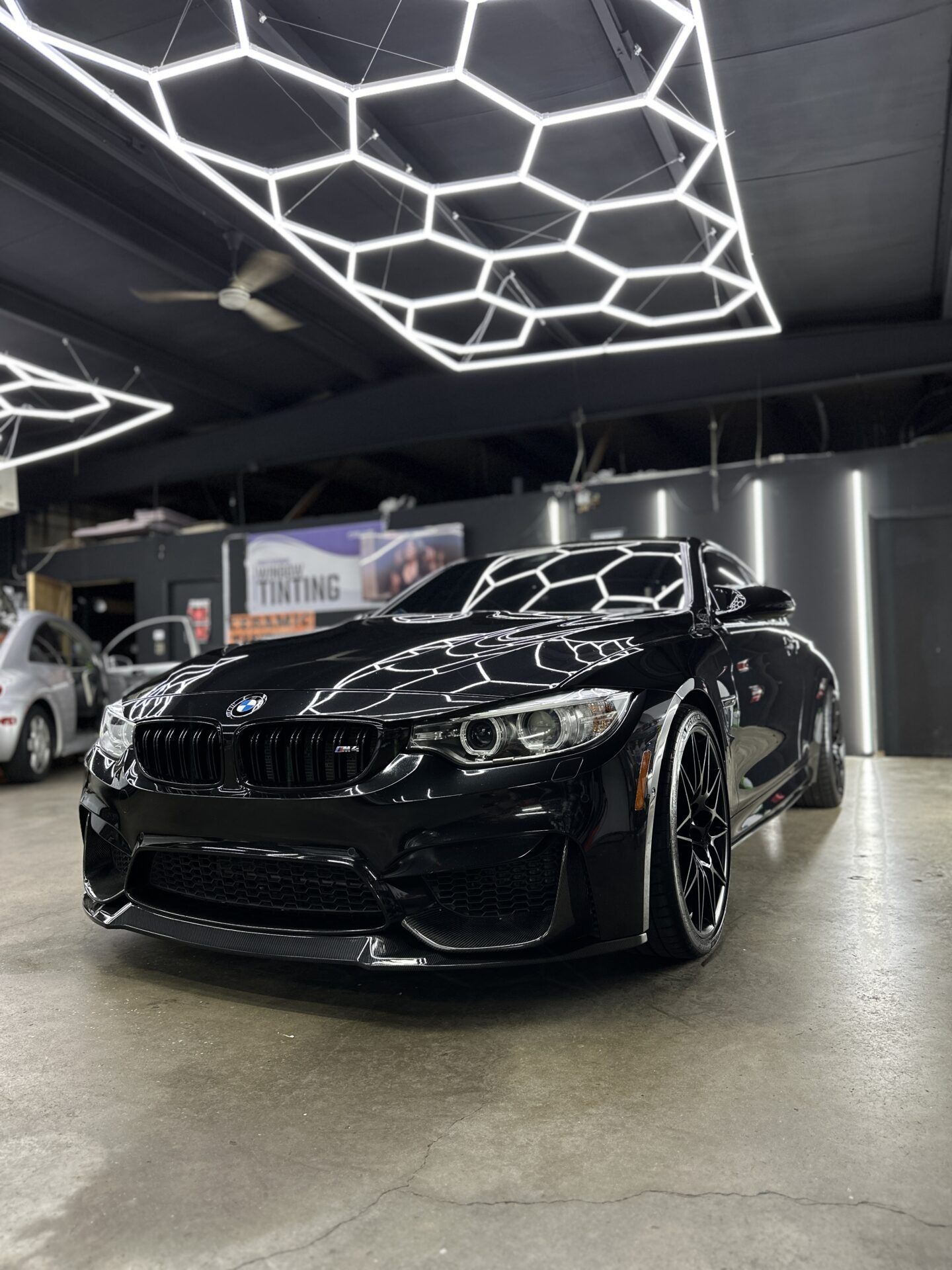 Black BMW coupe under hexagonal lights in a garage.
