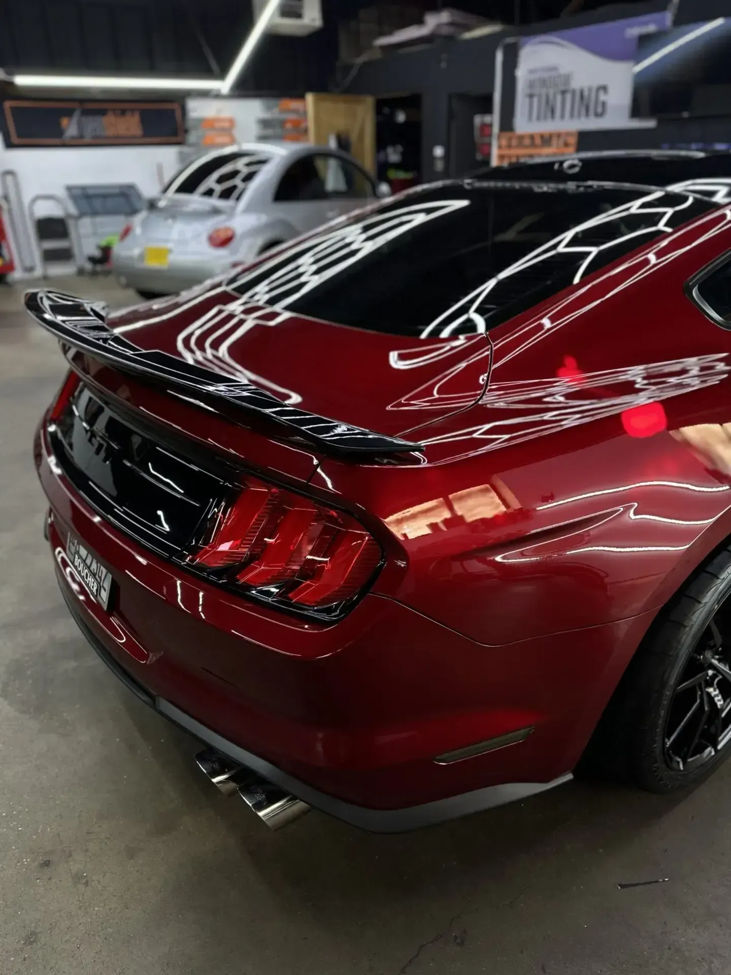 Red Mustang with black spoiler and tail lights, inside a shop.