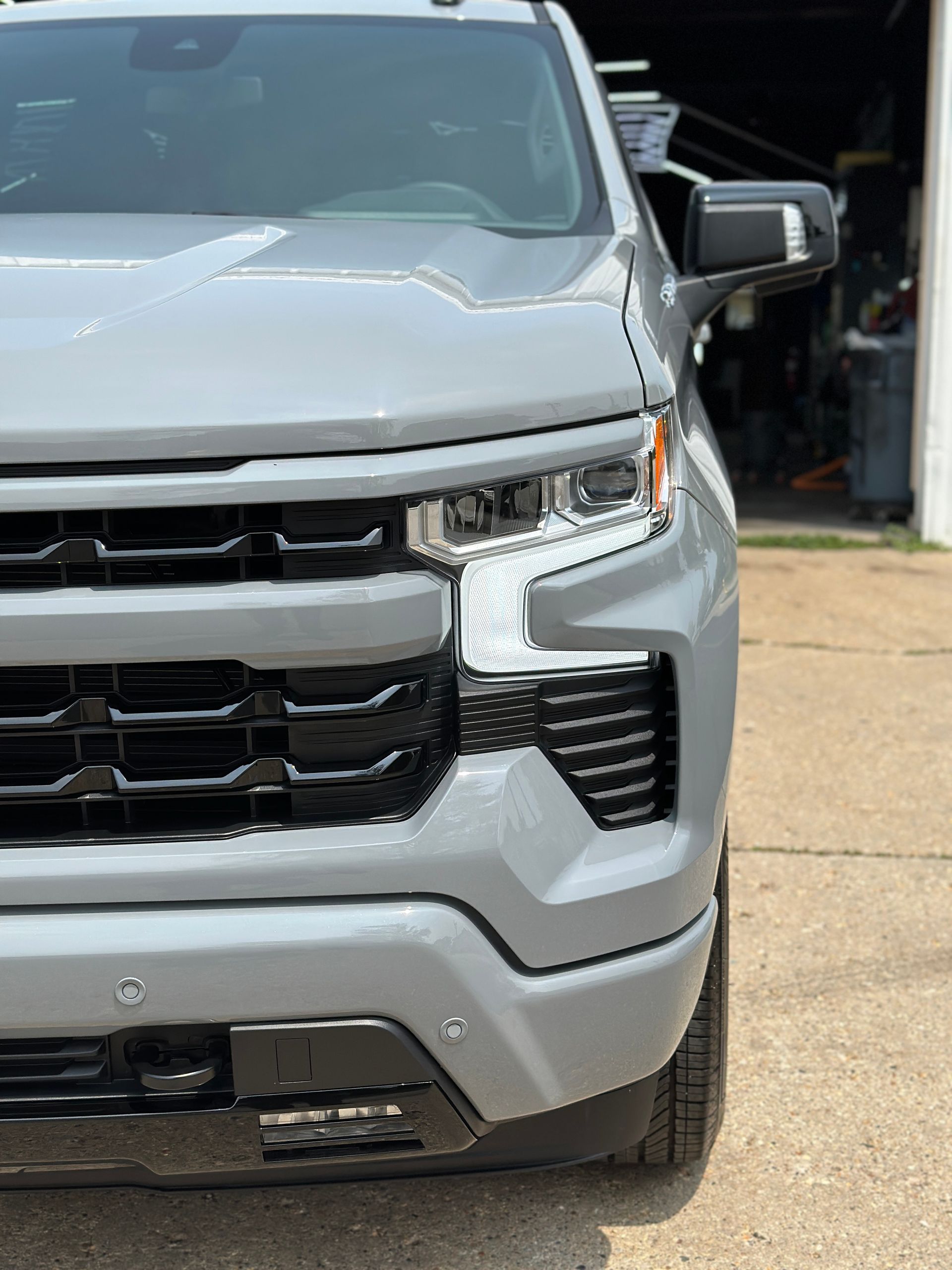 Gray Chevrolet Silverado truck, front view. Black grill, headlights. Daytime.