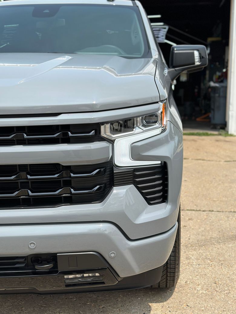 Gray Chevrolet Silverado truck, front view. Black grill, headlights. Daytime.