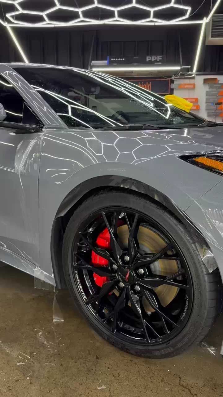 Gray sports car with black wheels, red brake calipers, and wet surface.