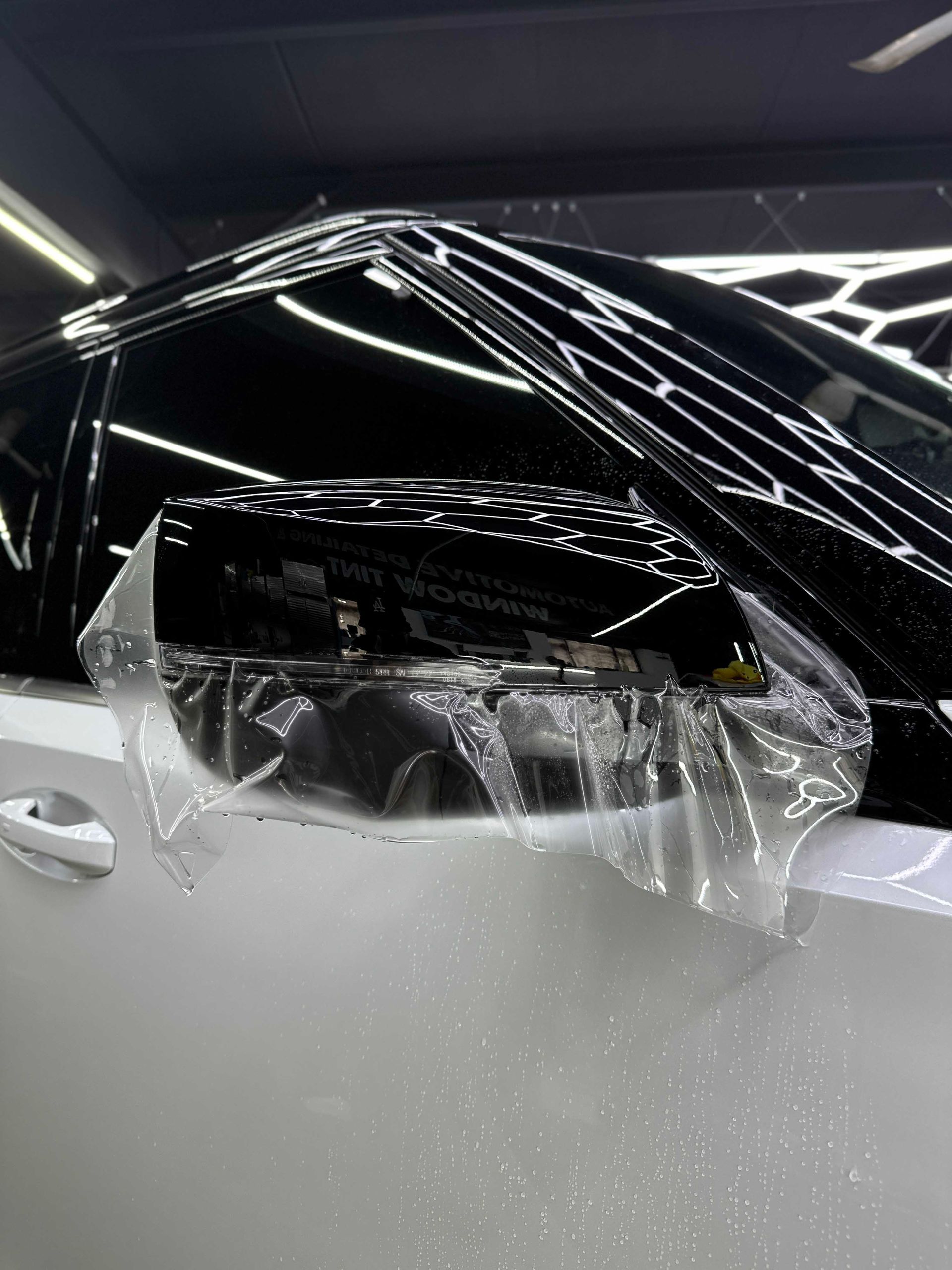 Clear film being applied to a black car mirror on a white car, likely for protection.