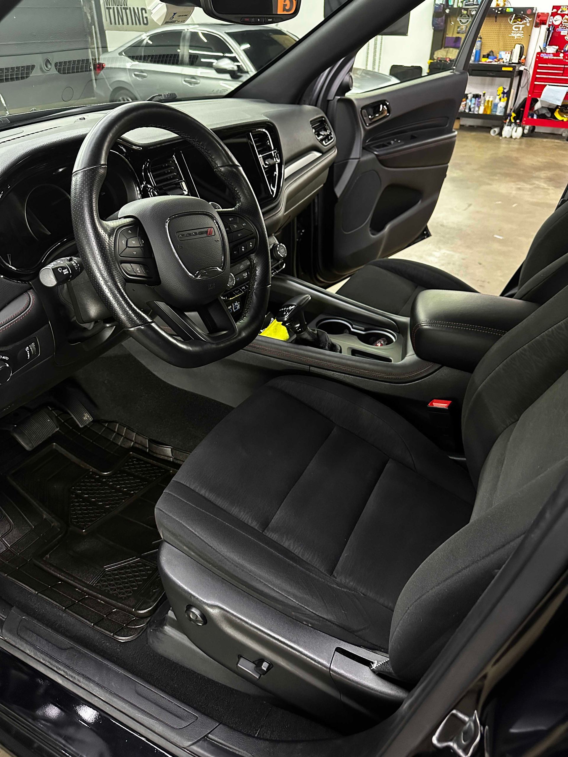 Black car interior: steering wheel, seat, dashboard, and floor mats.