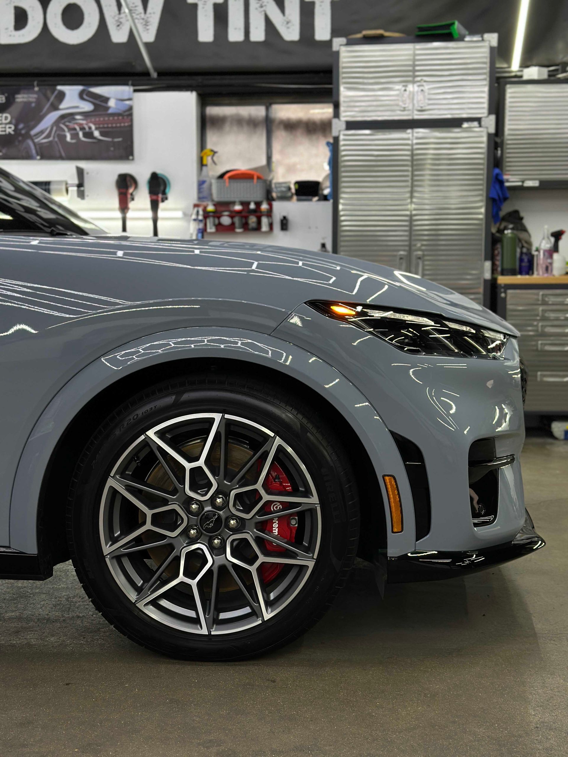 Gray Ford Mustang Mach-E front quarter view, black trim, red brake calipers, garage setting.