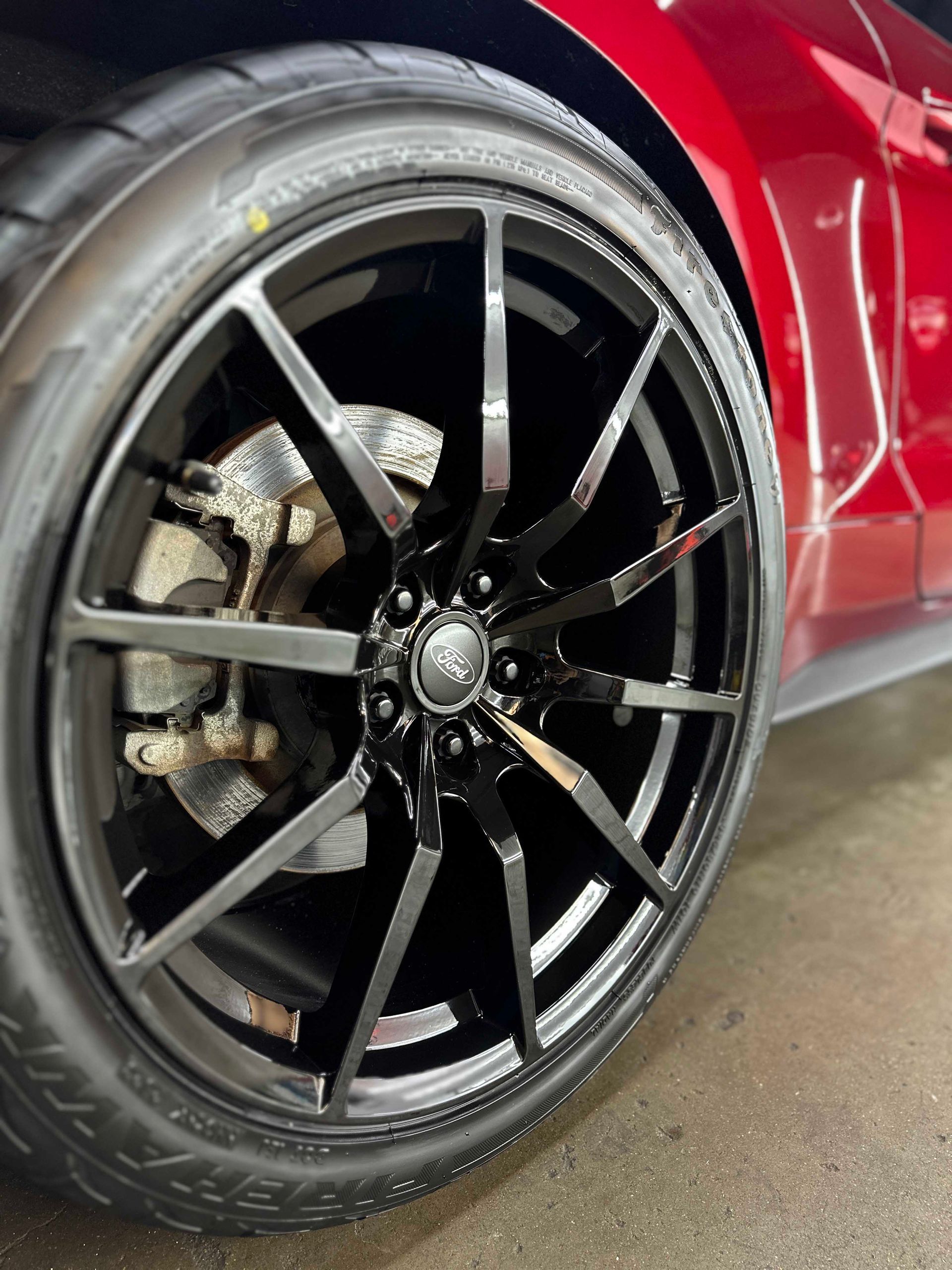 Black rim with tire on a red car; close-up view of the front wheel and brake.