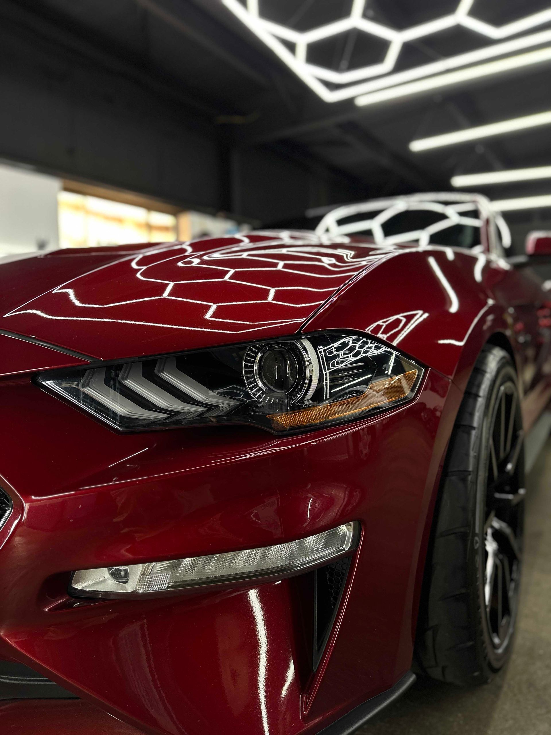 Red Ford Mustang, close-up view, with a glossy finish and black tires, in a brightly lit garage.