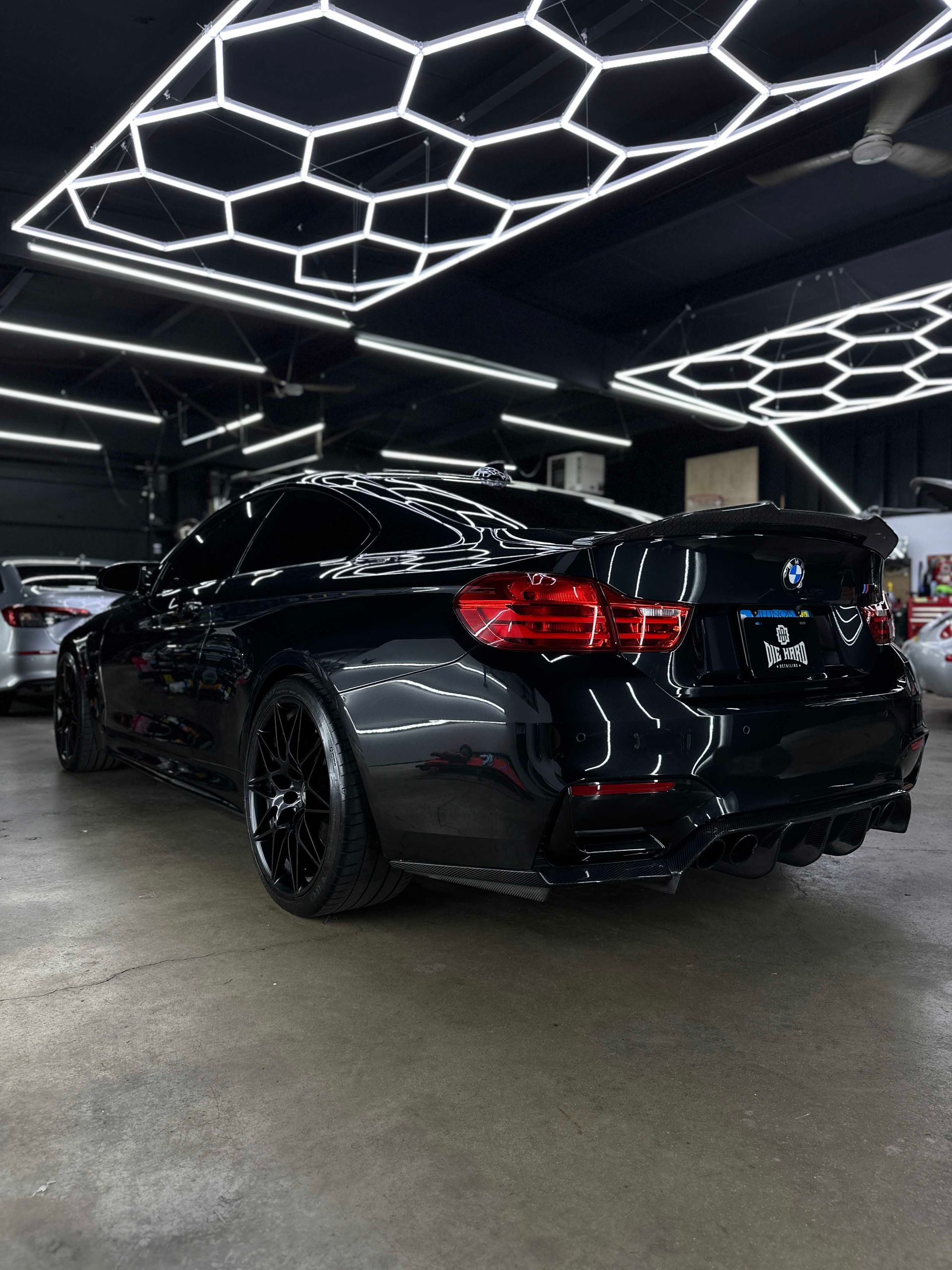 Black BMW M4 coupe in a car detailing shop, showcasing its shiny finish.