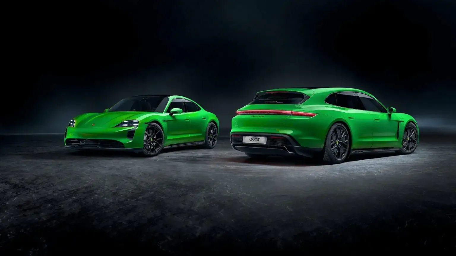 Two green Porsche Taycans, a sedan and a wagon, on a dark, textured surface.