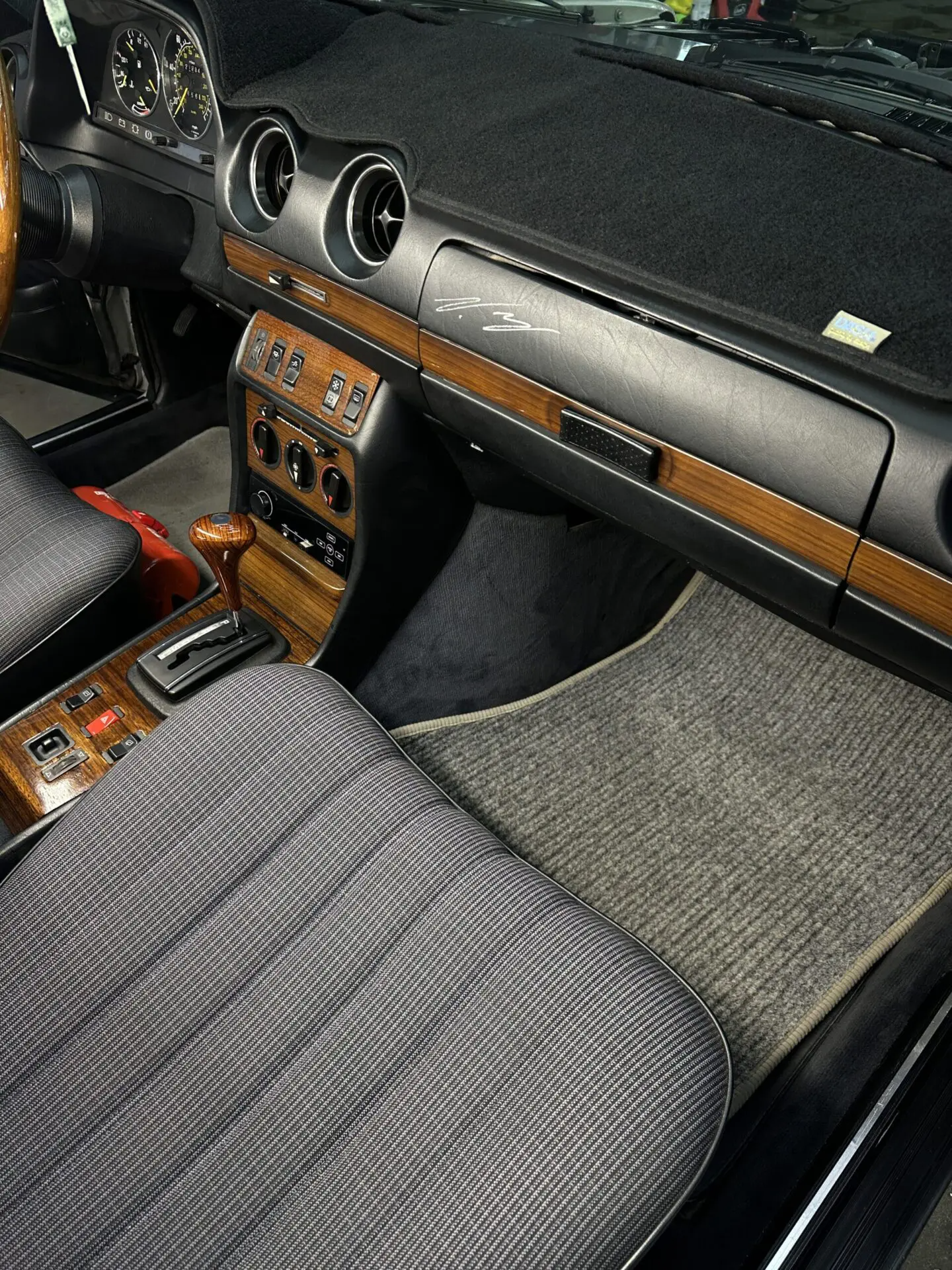 Interior of classic Mercedes-Benz: wood trim, black dashboard, gray seats, and gray carpet.