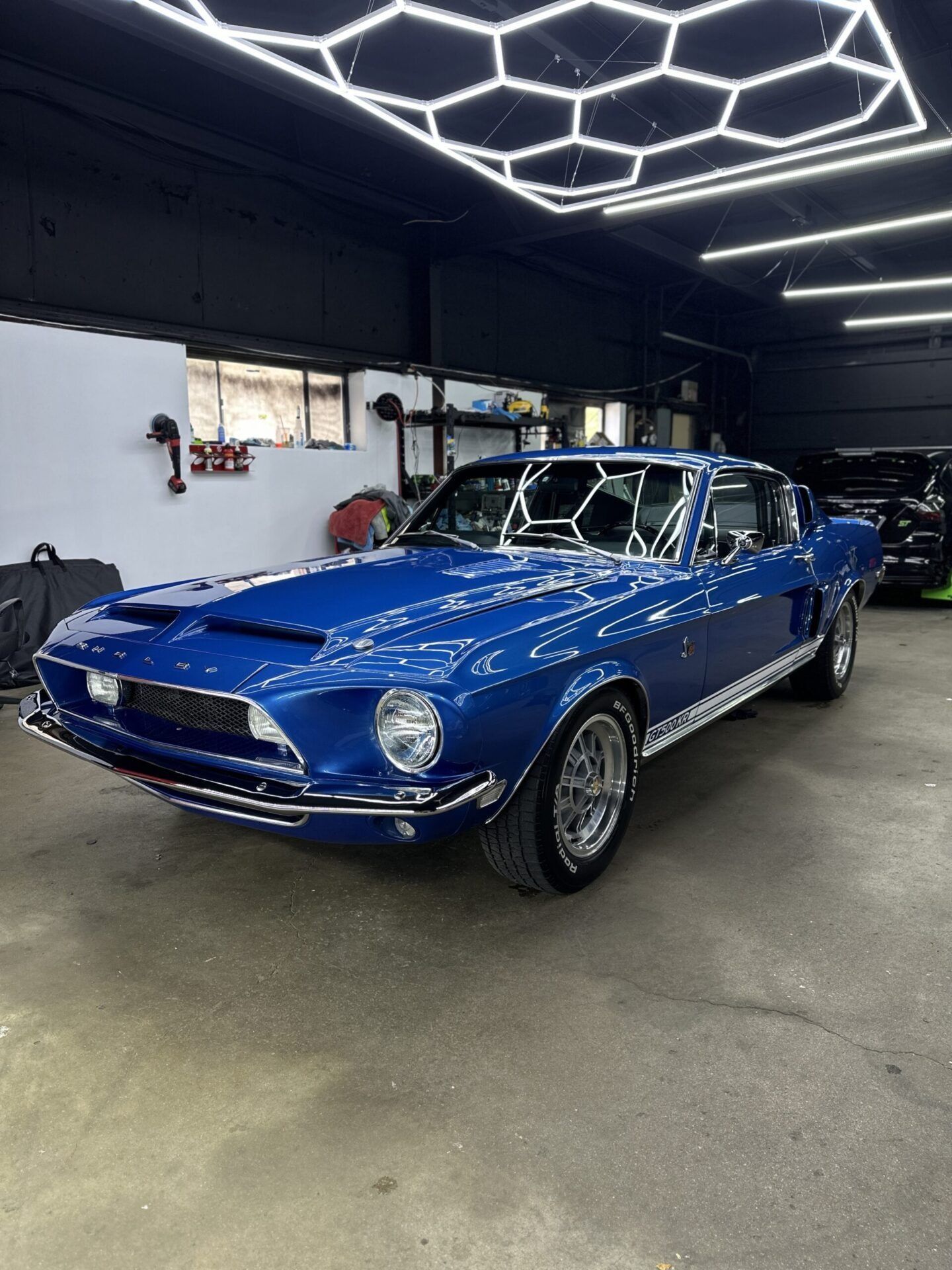 Blue vintage Shelby Mustang in a garage, parked under geometric lights.