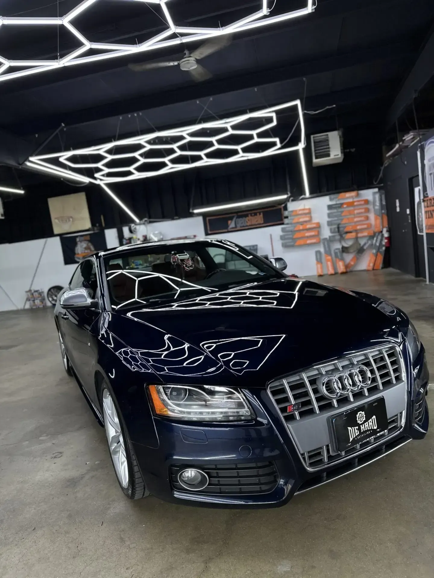 Dark blue Audi S5 in a garage with hexagonal lights overhead.