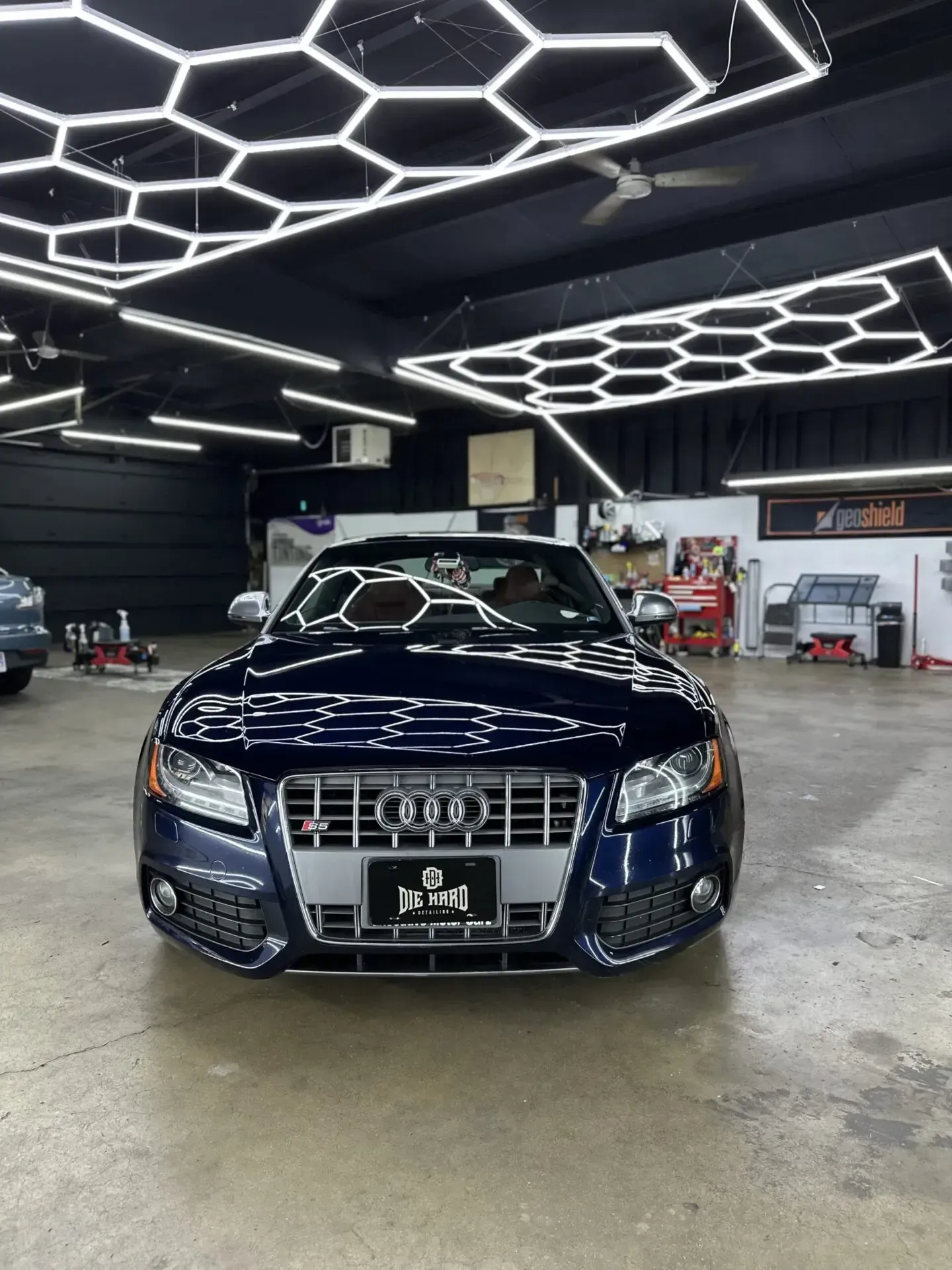Dark blue Audi S5 coupe parked inside a well-lit garage with hexagonal ceiling lights.