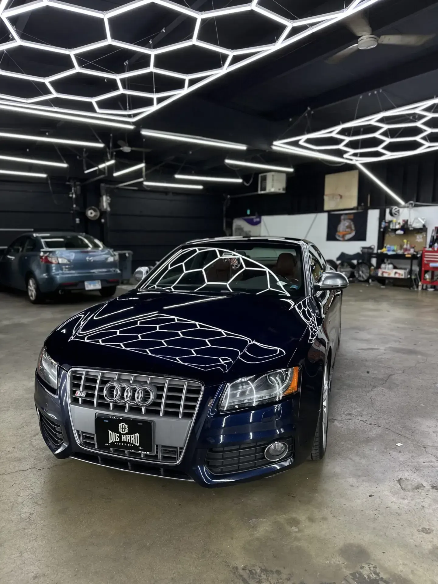 Dark blue Audi S5 under bright hexagonal lights in a car detailing shop.