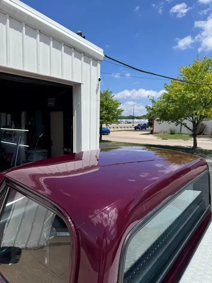 Burgundy pickup truck roof in front of a white building on a sunny day.