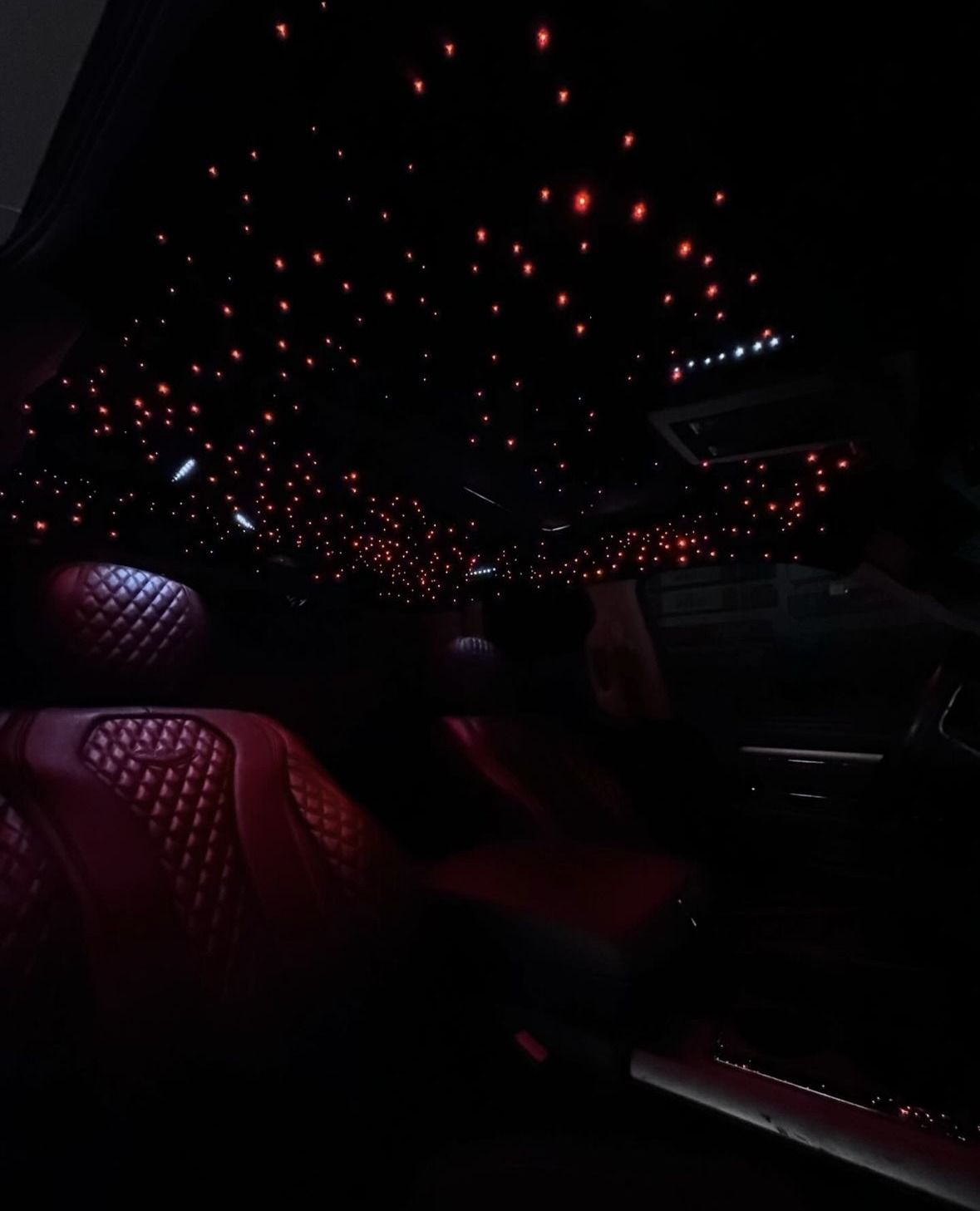 Red star-lit ceiling inside a car with red diamond-stitched seats. Dark setting.