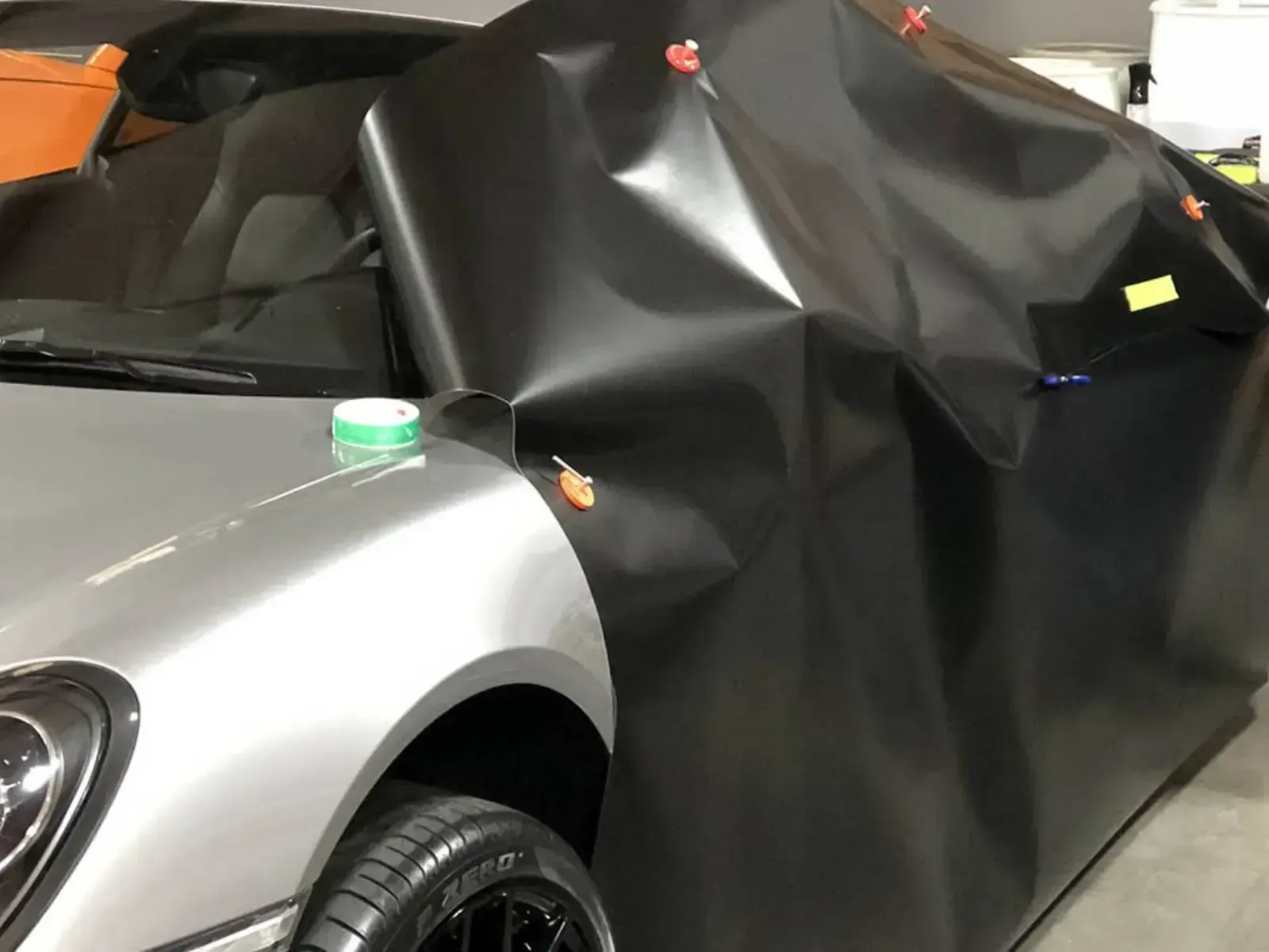 Silver sports car being wrapped in black vinyl, clips hold the material in place.