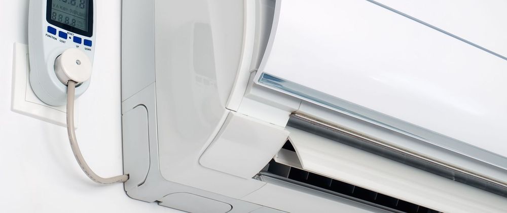 Close-up of a white air conditioner unit with a plug connected to a power meter on a wall.