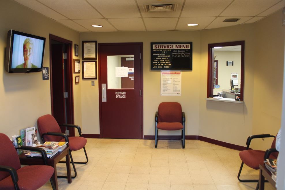 Waiting room with maroon chairs, TV, and service window. Beige walls, brown doors, and a tiled floor.