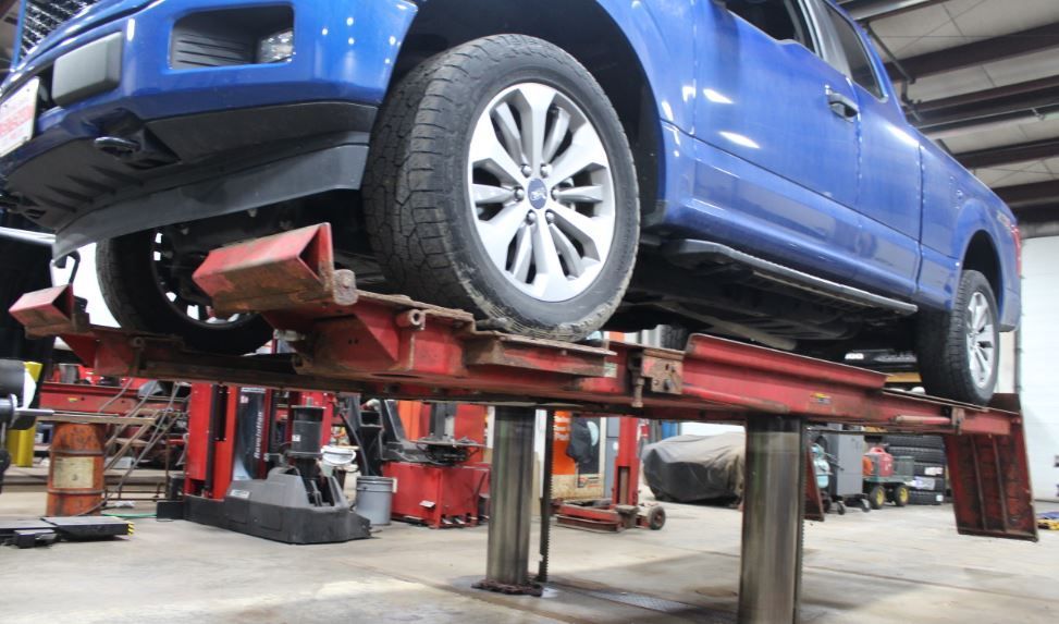 Blue car raised on a red hydraulic lift inside a garage.