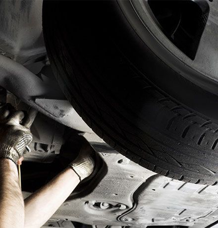 Hands wearing gloves working under a car near a tire.