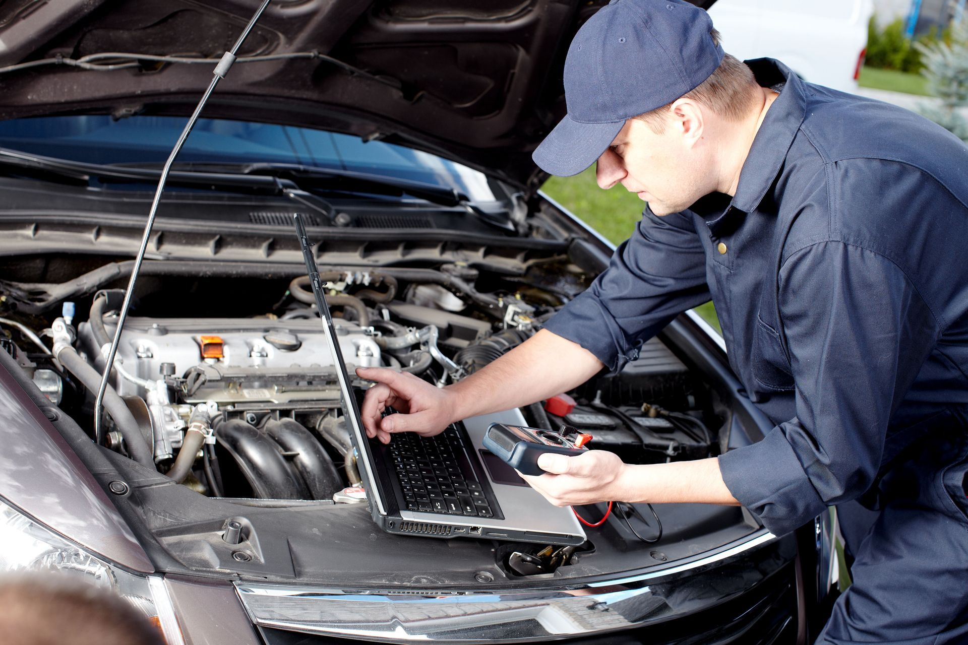 Mechanic in blue uniform uses laptop to diagnose a car engine.