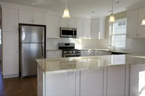 Bright white kitchen with stainless steel appliances and a granite island under pendant lights