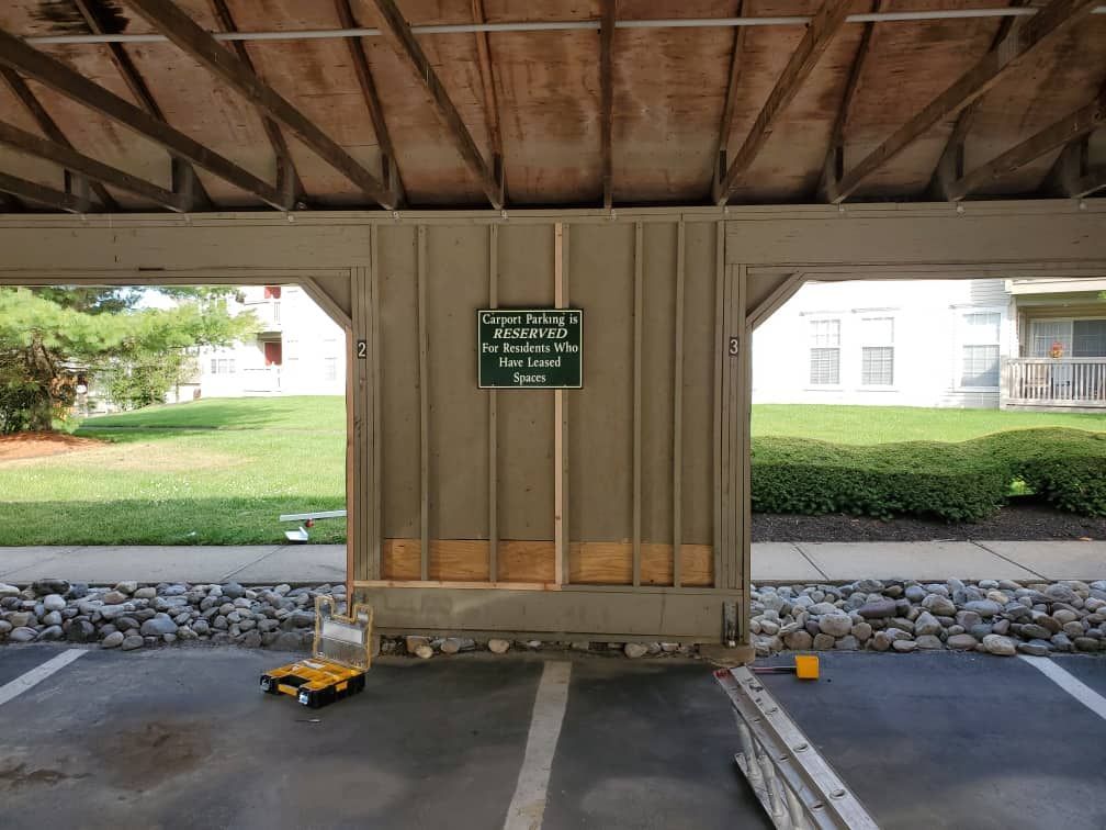 Parking area under a covered structure with a green sign on a wall and a yellow wheelchair ramp at left