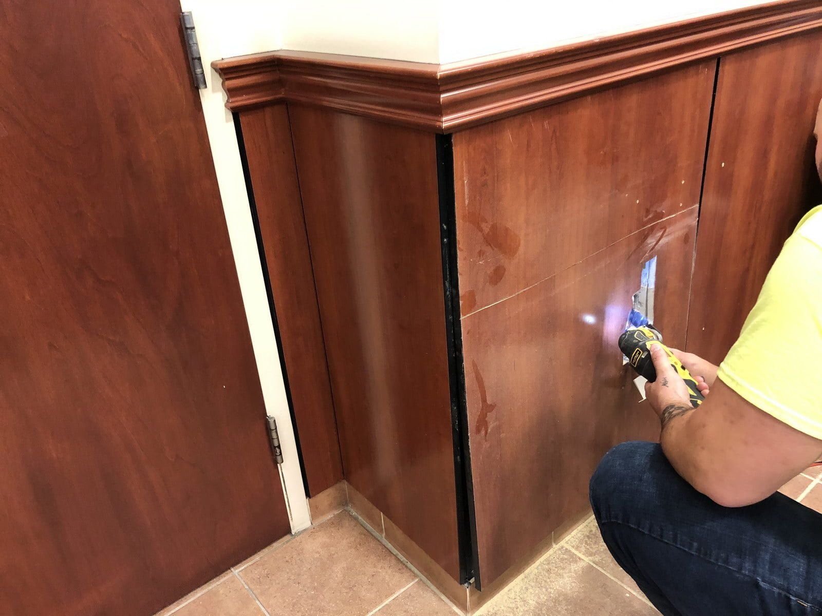 Person painting or repairing a wooden cabinet corner with a small tool indoors.