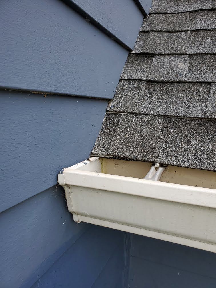 Damaged roof gutter at a house corner with white trim and blue siding