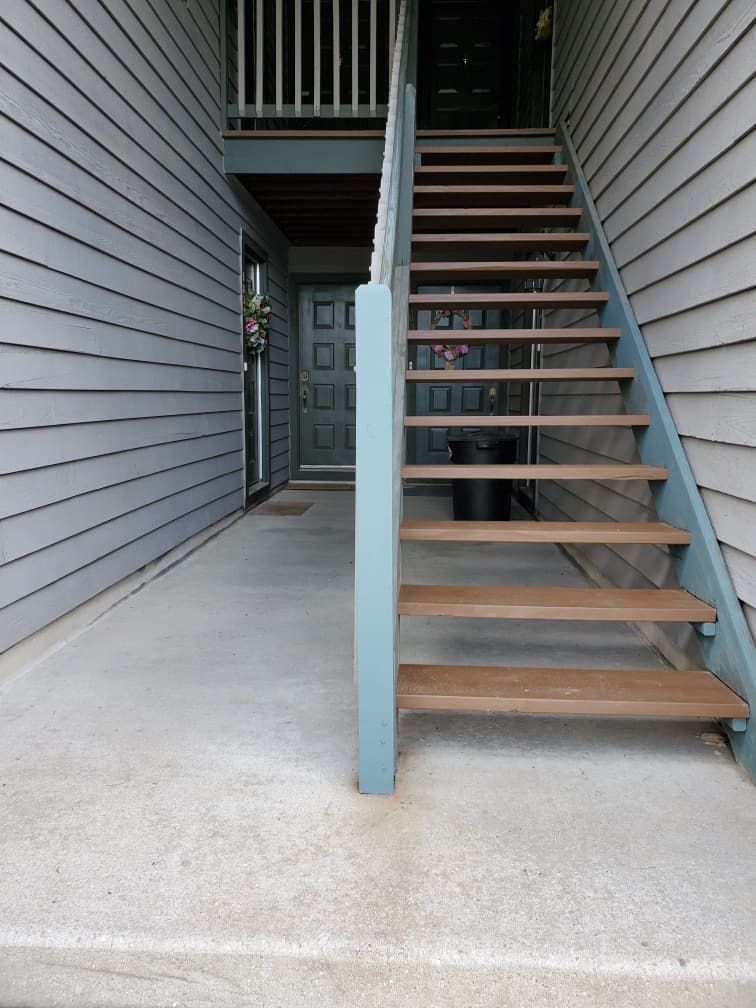Exterior apartment staircase with gray siding, concrete landing, and wooden steps leading to a door