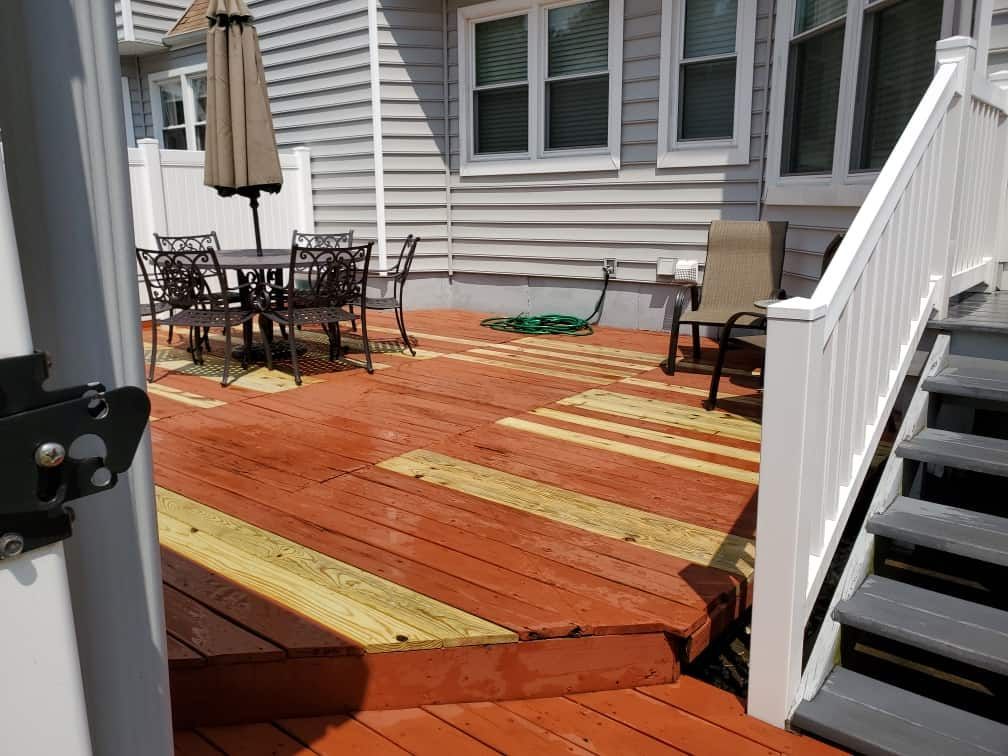 Wooden backyard deck with orange stain, patio table and chairs, umbrella, and white stairs.