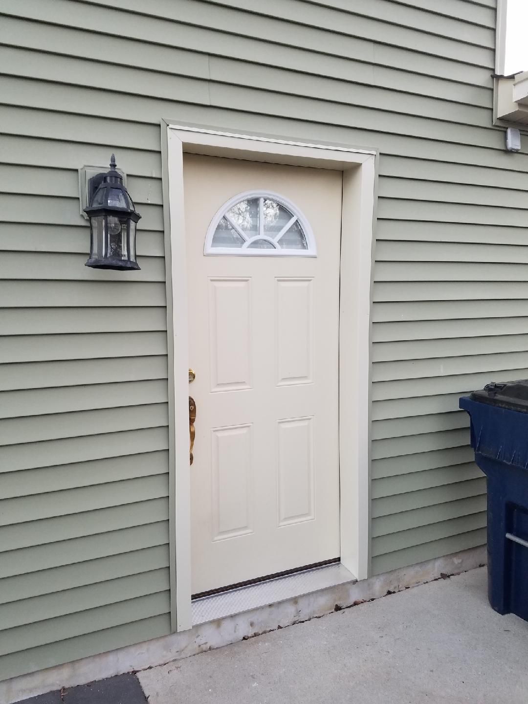 Front door of a house with white trim, green siding, a lantern, and a blue trash bin nearby.