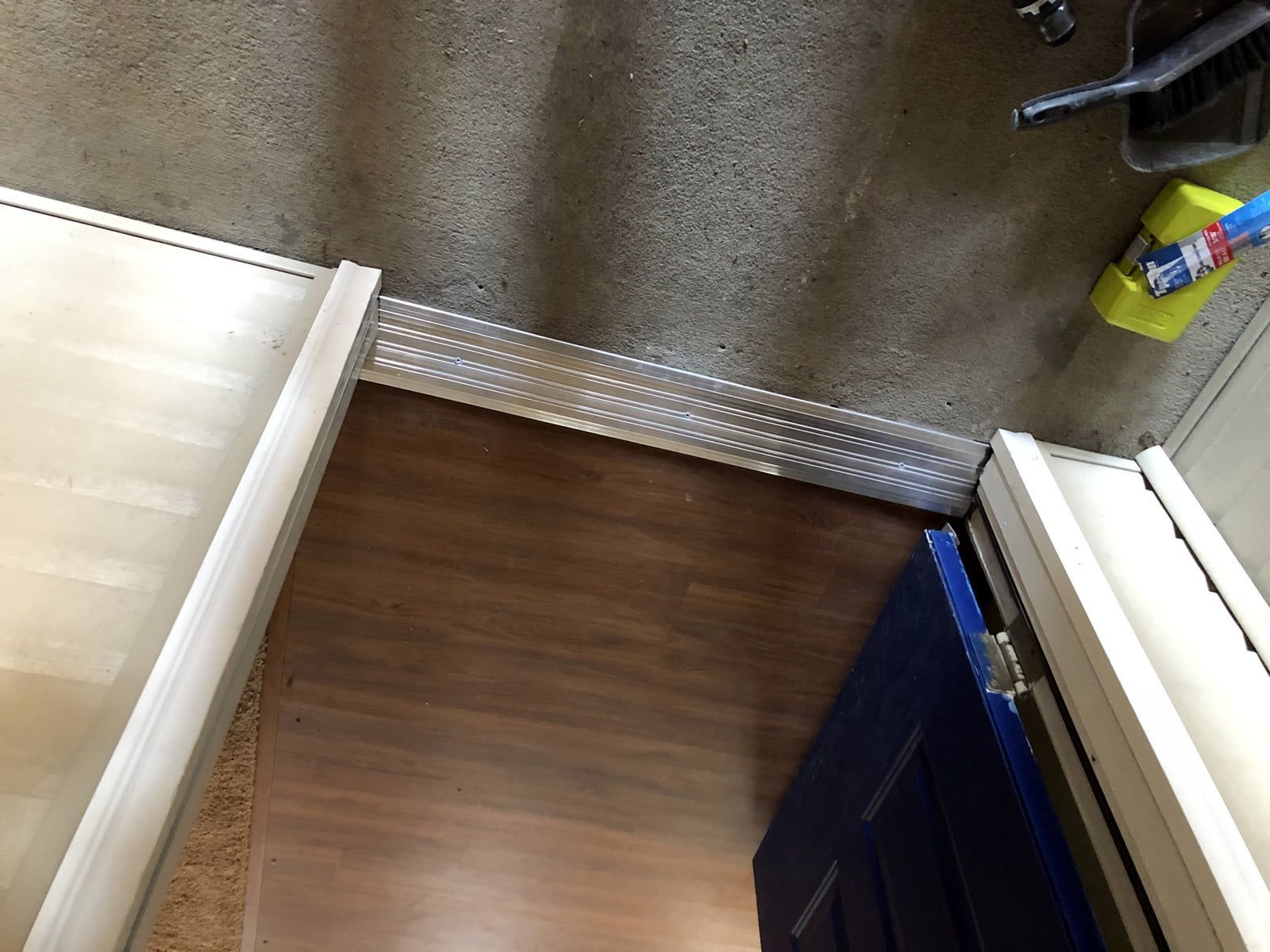 Narrow gap between two beds, with a brown floor and a wall-mounted outlet or fixture.