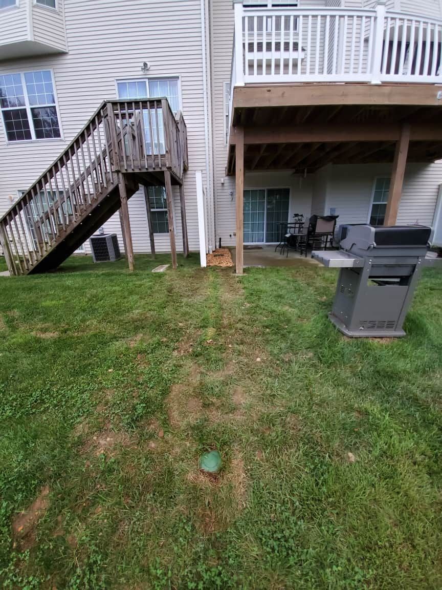 Backyard with wooden stairs to a deck, patio furniture, and a grill on grass with a worn path