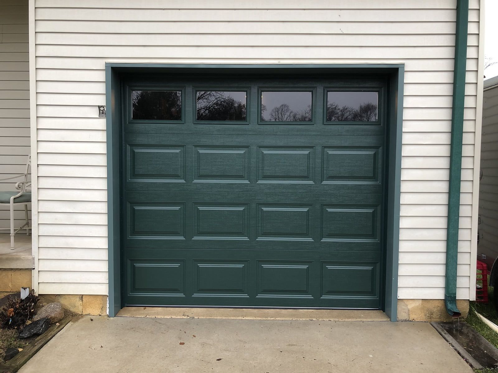 Dark green garage door on a house exterior with white siding and small upper windows
