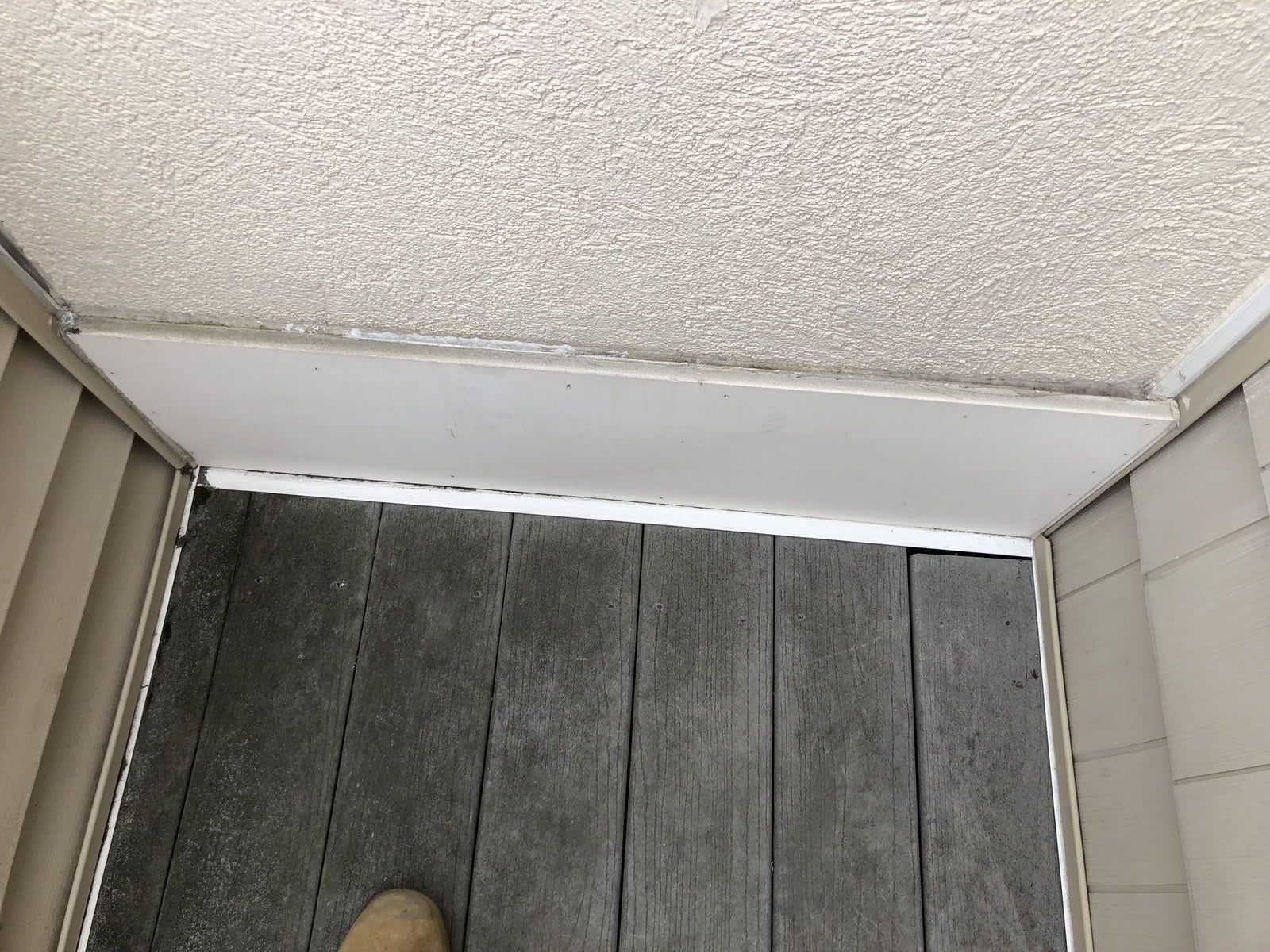 Upward view of a textured ceiling corner above a gray deck floor with white trim