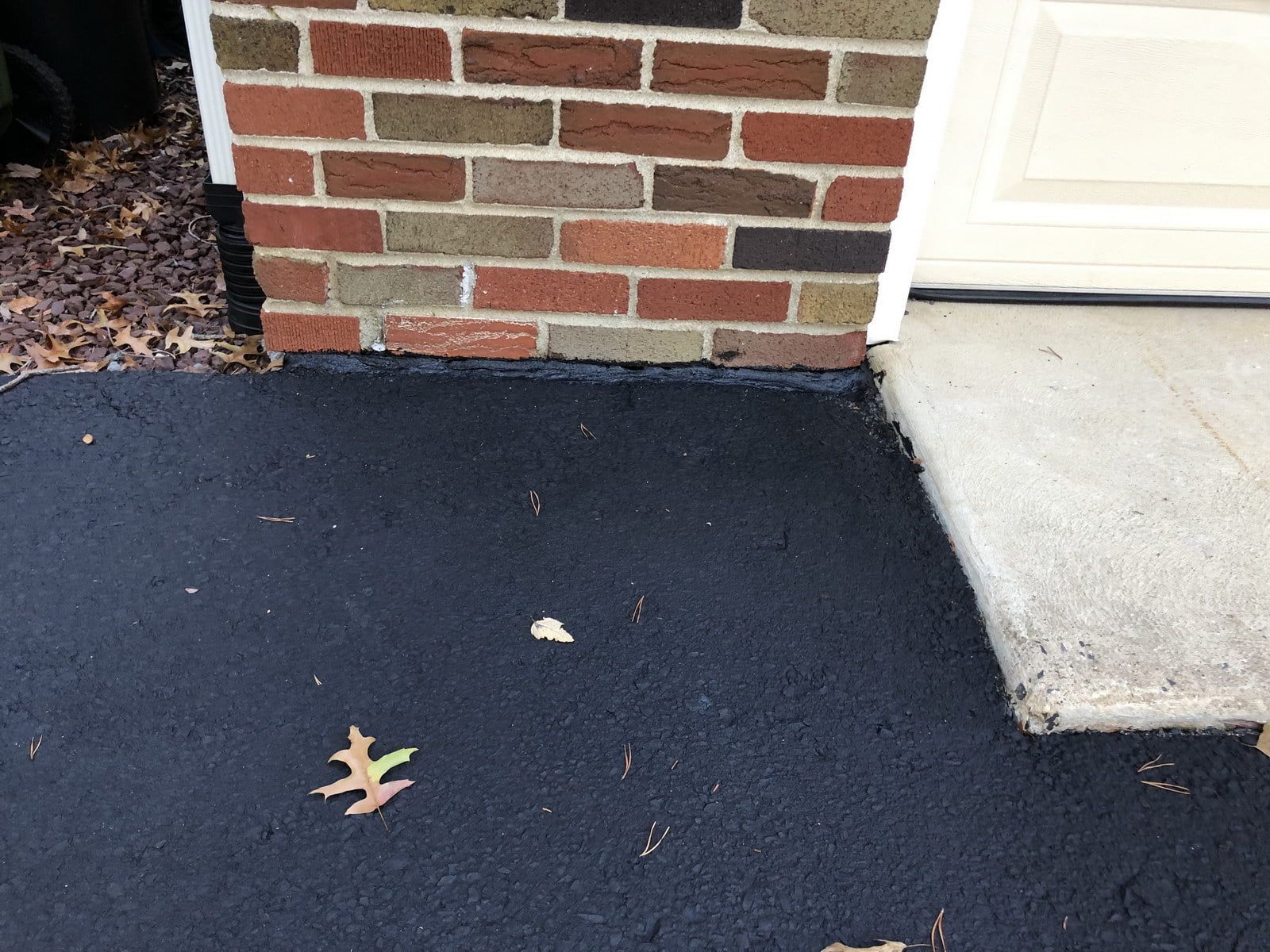 Brick wall beside a concrete step and black asphalt with a few fallen leaves