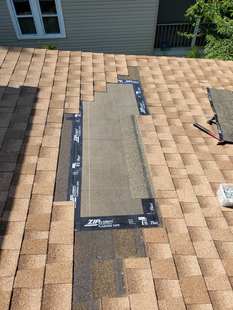Roof shingle repair with a rectangular patch of roofing felt on a tan shingled roof.