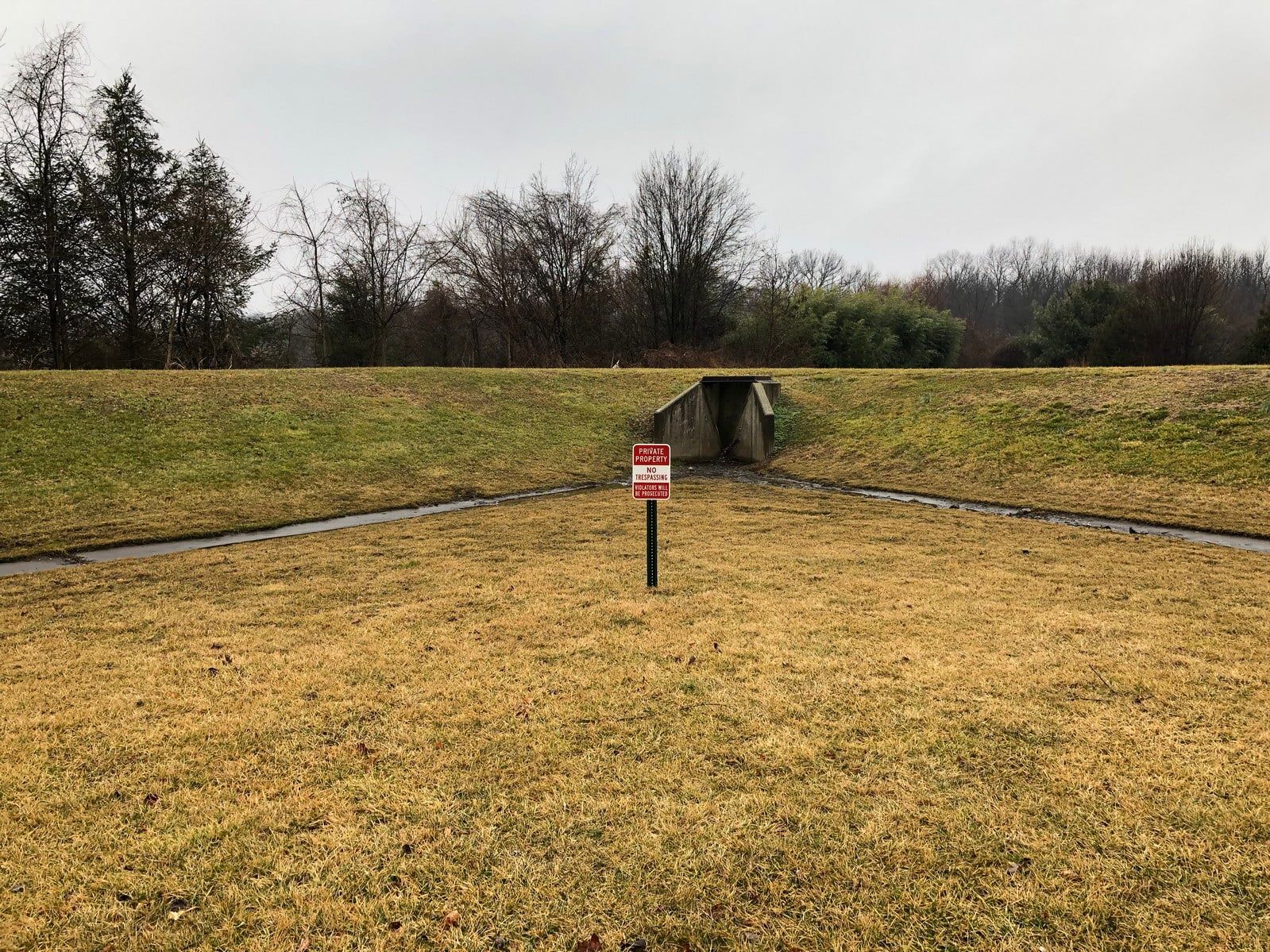 Grassy field with a small tunnel in the distance and a red warning sign in the center